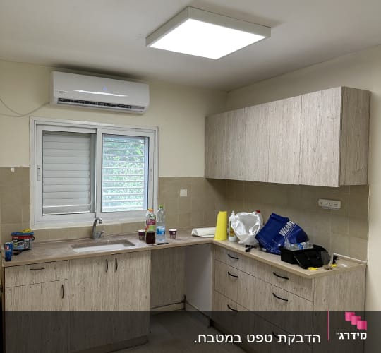 מטבח עם ארונות עץ, כלים וחומרי ניקוי על השיש